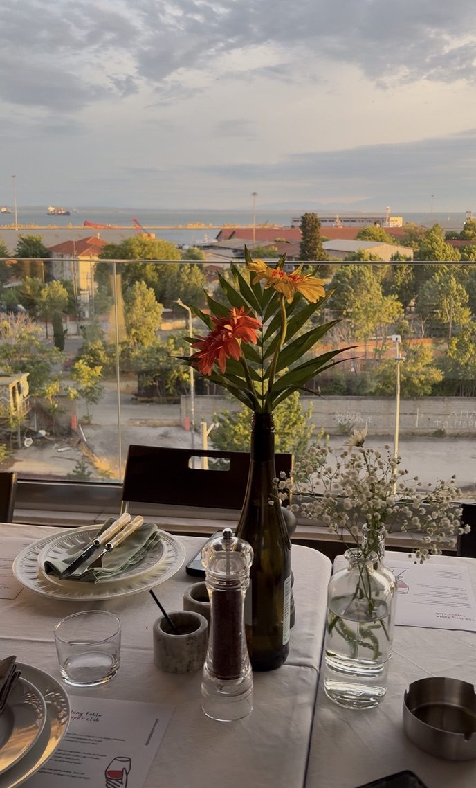 flowers and a bottle on the table with the port in the distance